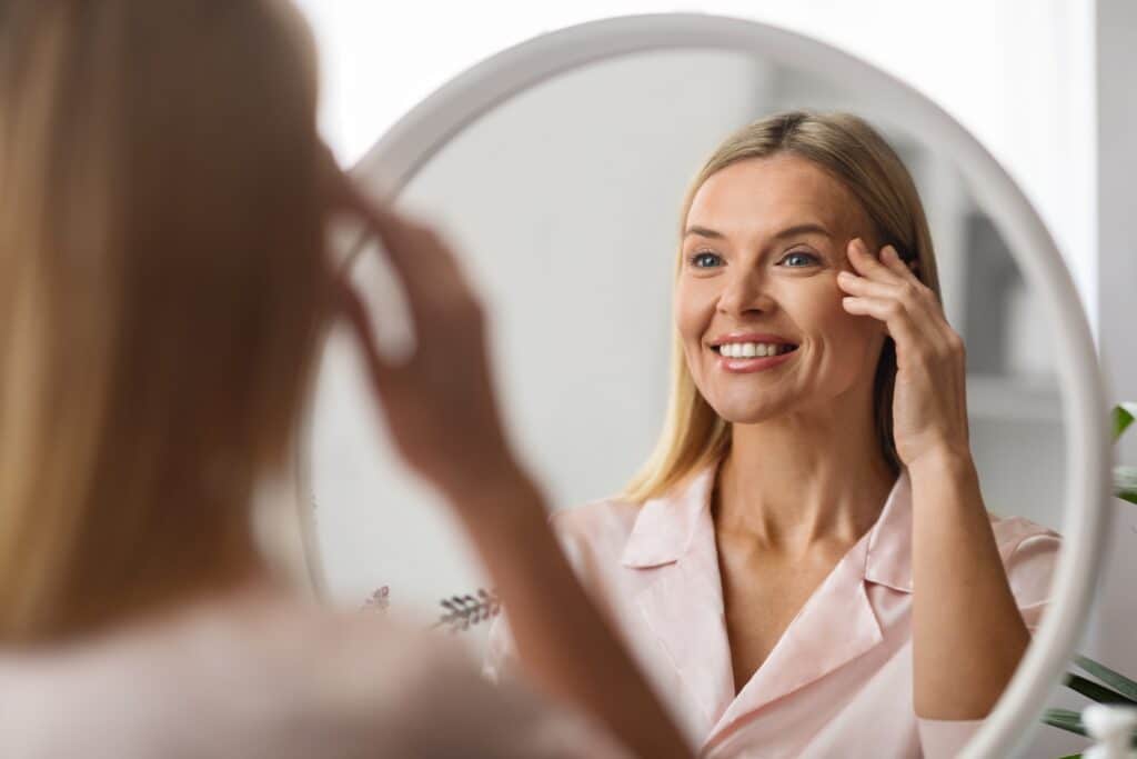 Cheerfulmaturewomanlookingatmirrorathomeapplyingeye - Visionmax Eye Centre
